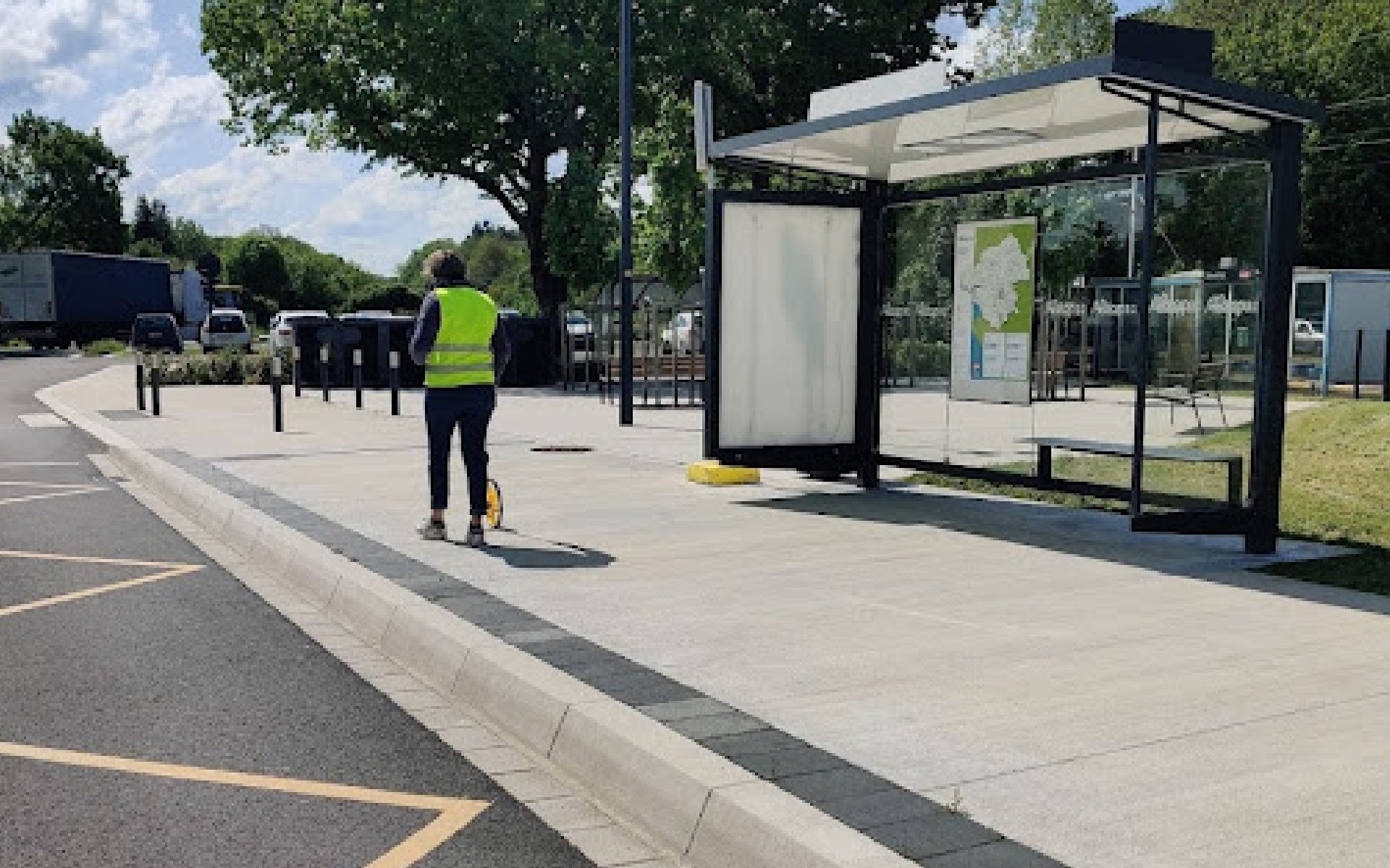 Personne en gilet fluorescent près d'un arrêt de bus avec abri vitré et plan affiché