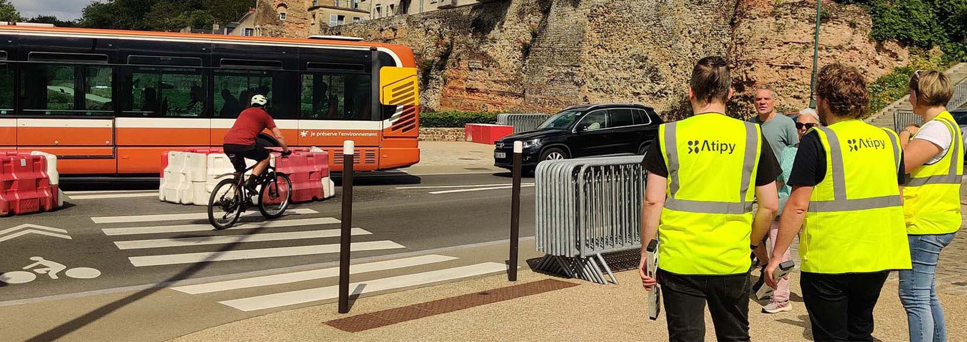 Personnes en gilet Atipy observant un passage piéton et une voie cyclable devant un bus orange