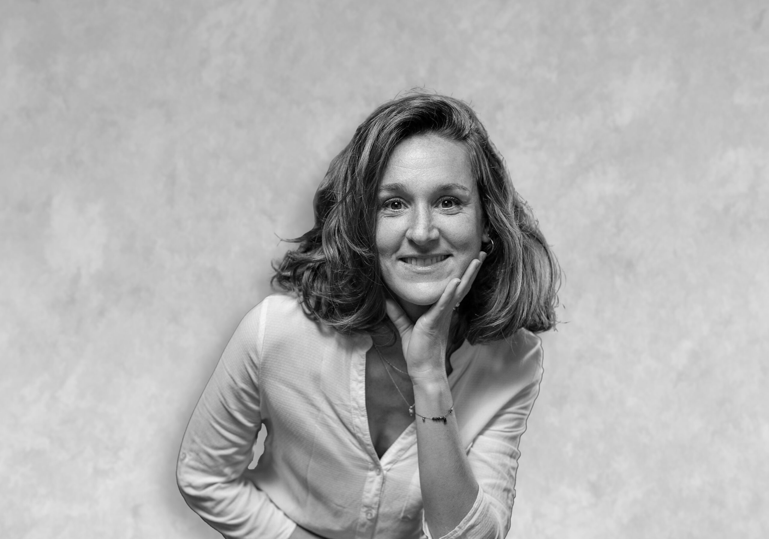adeline Portrait d’une femme aux cheveux mi-longs en chemise claire, appuyée sur sa main devant un fond uni