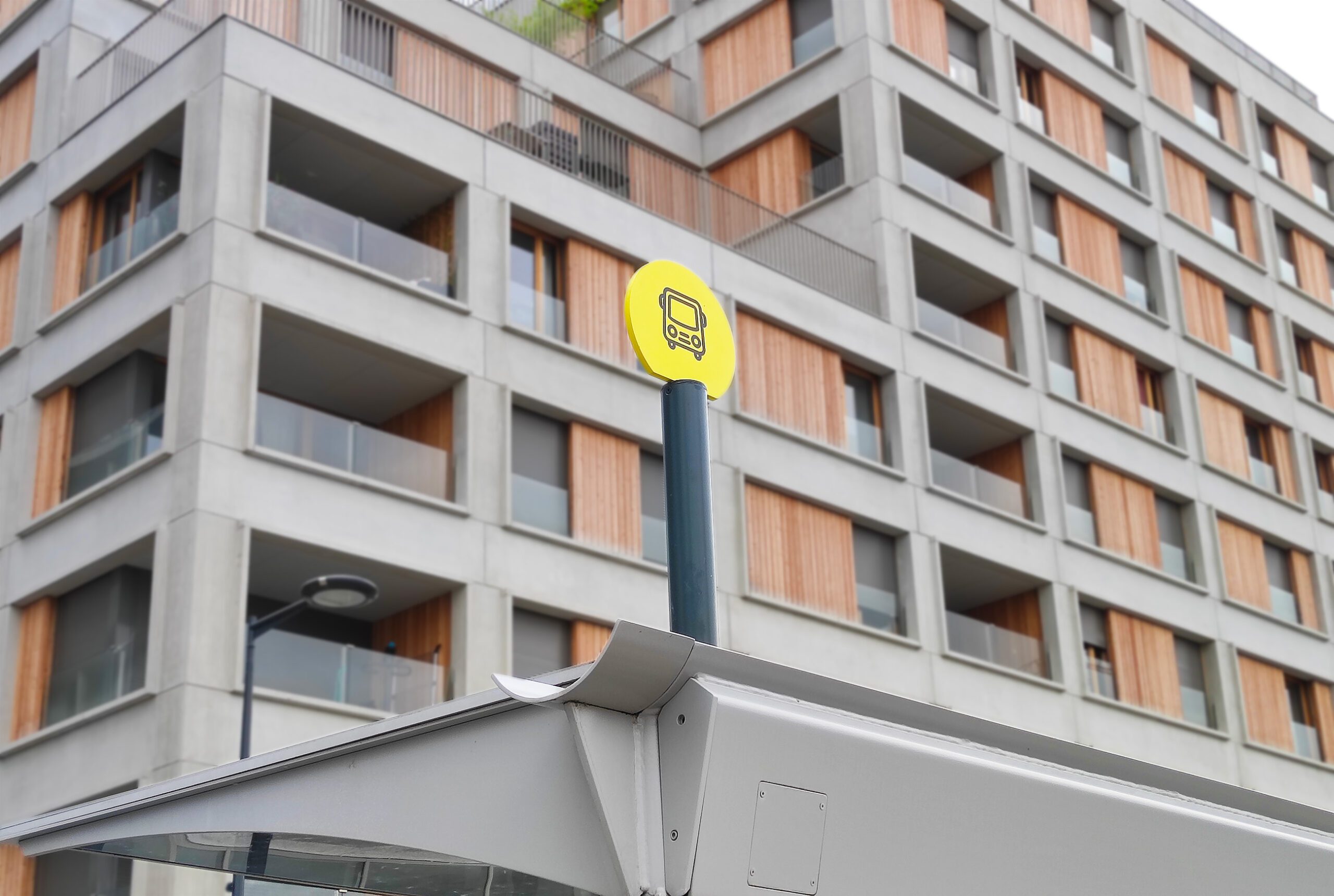 Pictogramme jaune d’arrêt de tramway sur un abri, devant la façade d’un immeuble contemporain à balcons