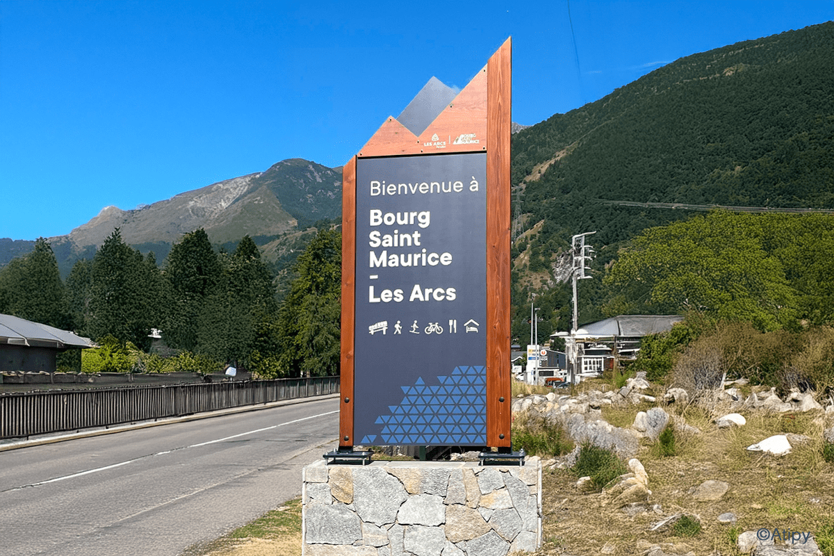 Totem de bienvenue Bourg Saint Maurice Les Arcs au bord d'une route, avec montagnes en arrière-plan