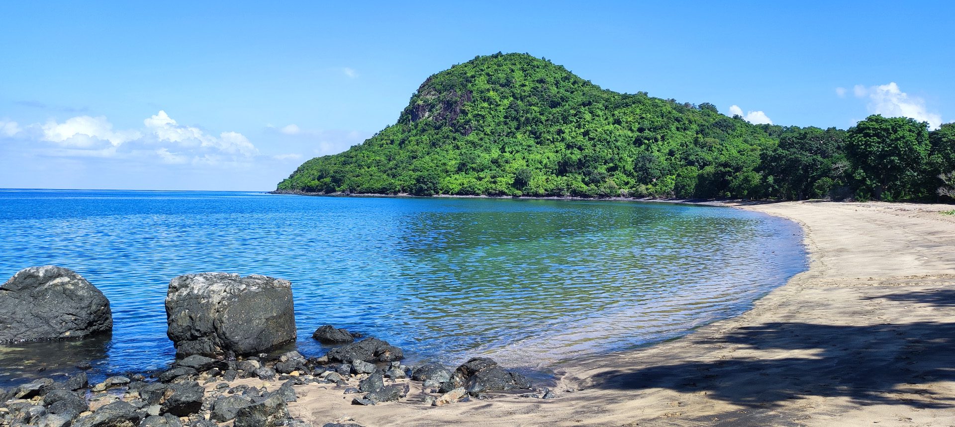 Plage de sable bordée d'une mer calme et d'une colline verdoyante sur le littoral de Mayotte
