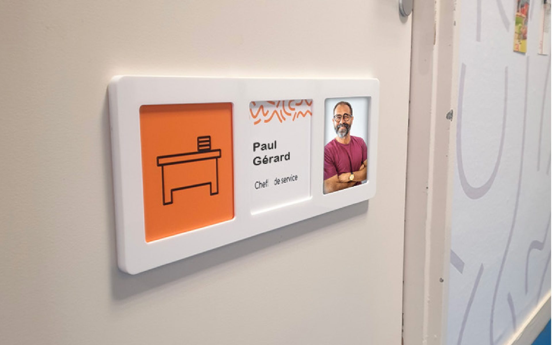 Plaque signalétique de porte avec pictogramme bureau, nom Paul Gérard, fonction chef de service et portrait flouté