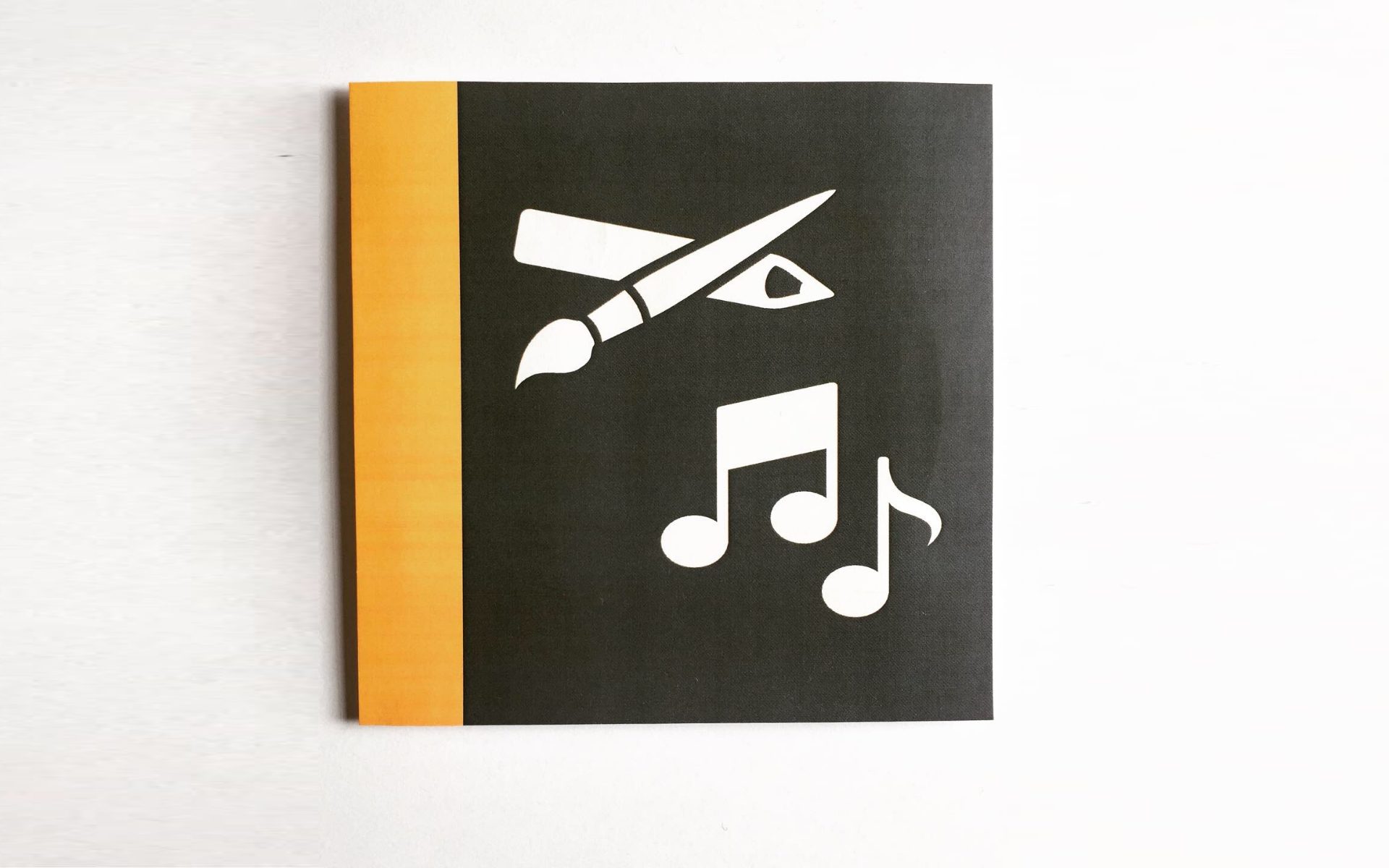 Panneau noir avec bande jaune montrant un pinceau, une équerre et des notes de musique en blanc
