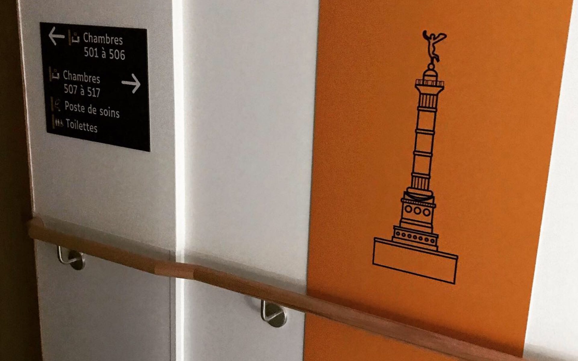 Panneau directionnel pour chambres, poste de soins et toilettes à côté d'un mur orange avec colonne dessinée