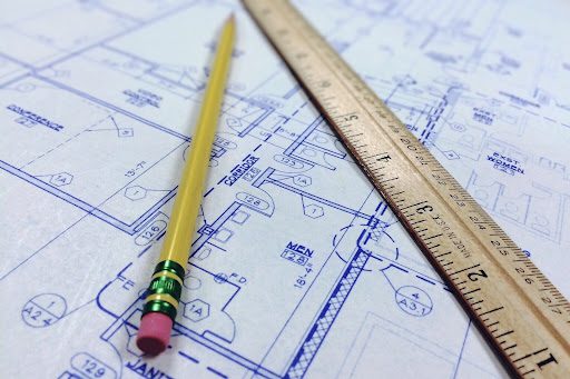 Crayon jaune et règle en bois posés sur un plan architectural avec cotes et annotations techniques