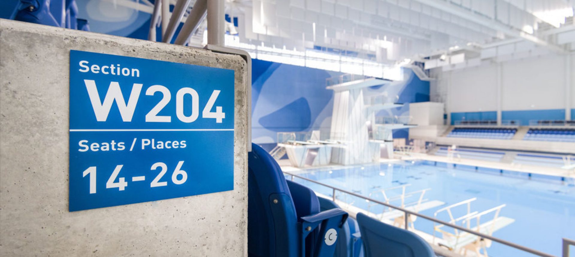 Panneau bleu Section W204, Seats / Places 14-26 fixé en tribune devant un bassin de plongeon intérieur