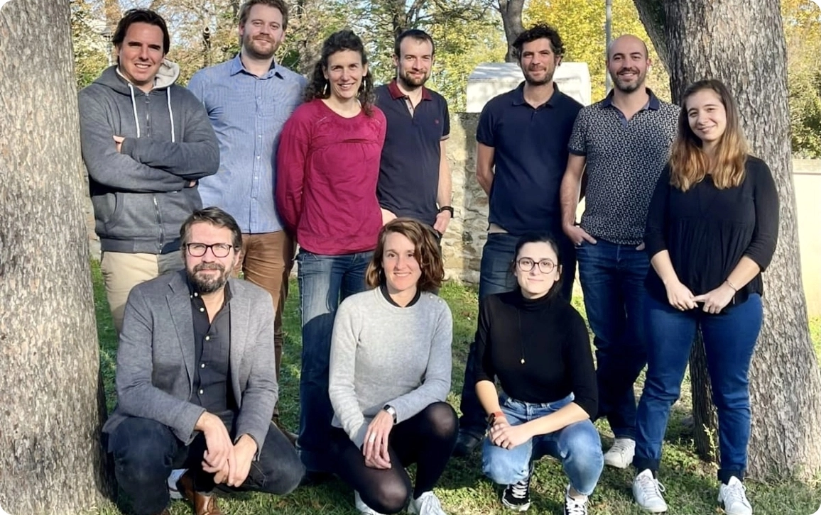 Neuf membres de l’équipe posent en extérieur entre des arbres, certains debout et d’autres accroupis