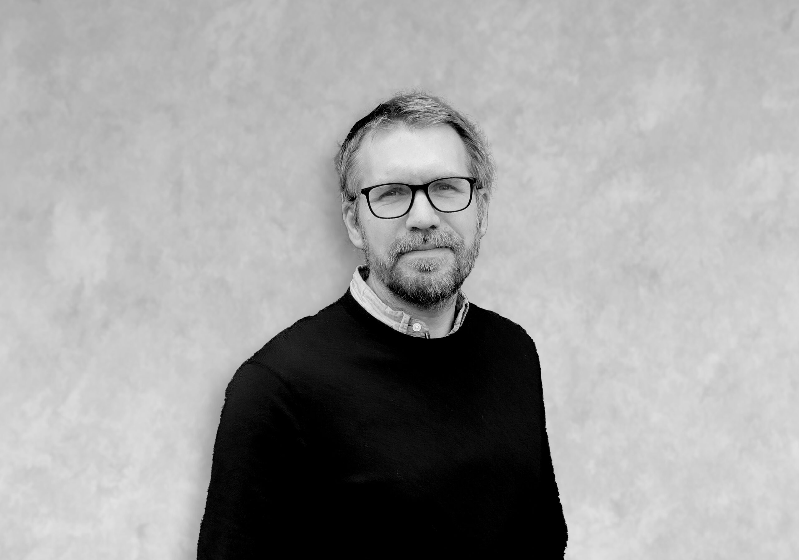 guillaume Portrait de Guillaume, homme en pull sombre devant un mur clair texturé, visage volontairement masqué