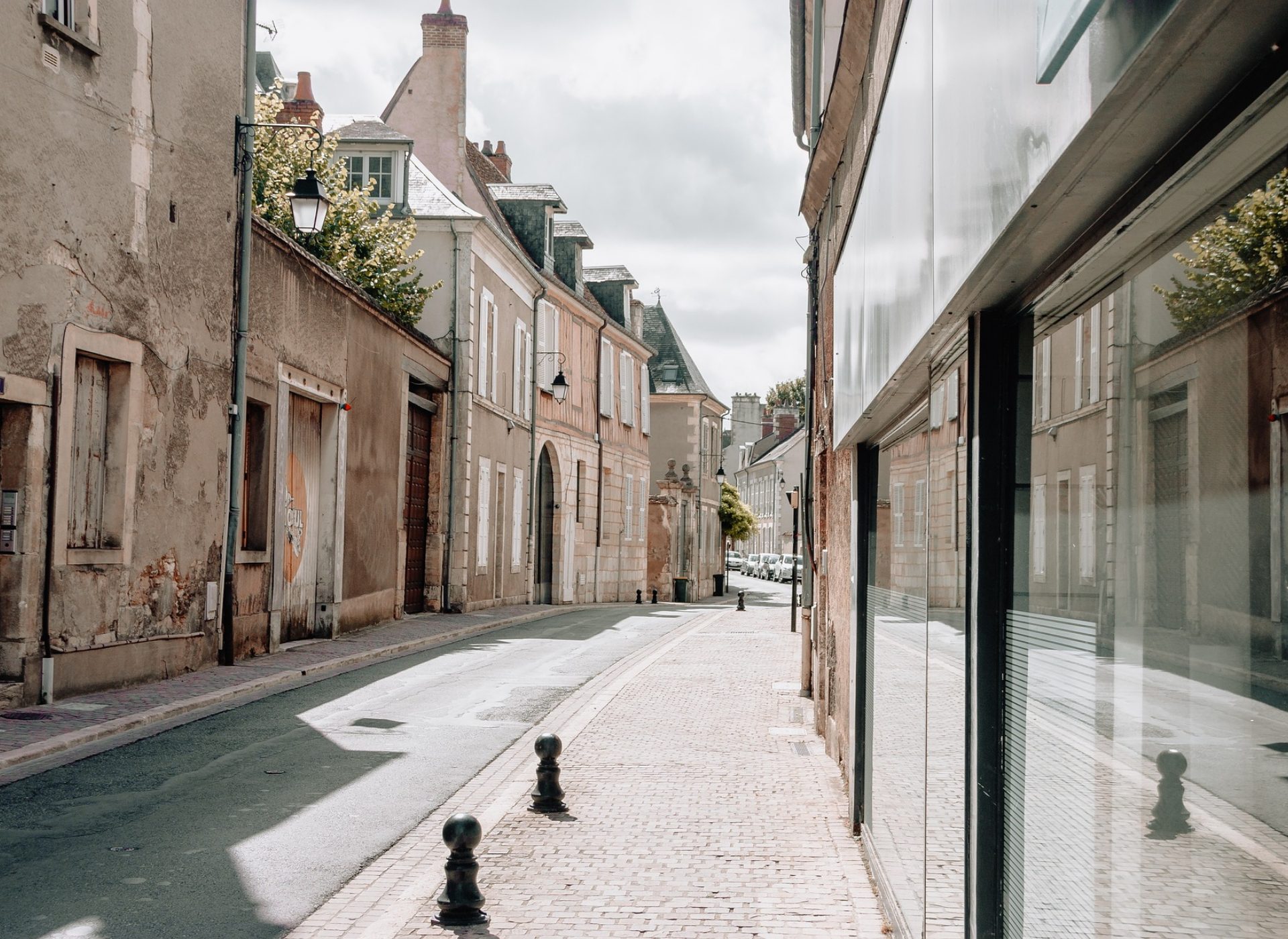 Rue étroite en centre-ville avec trottoir pavé, bornes noires et façades anciennes alignées