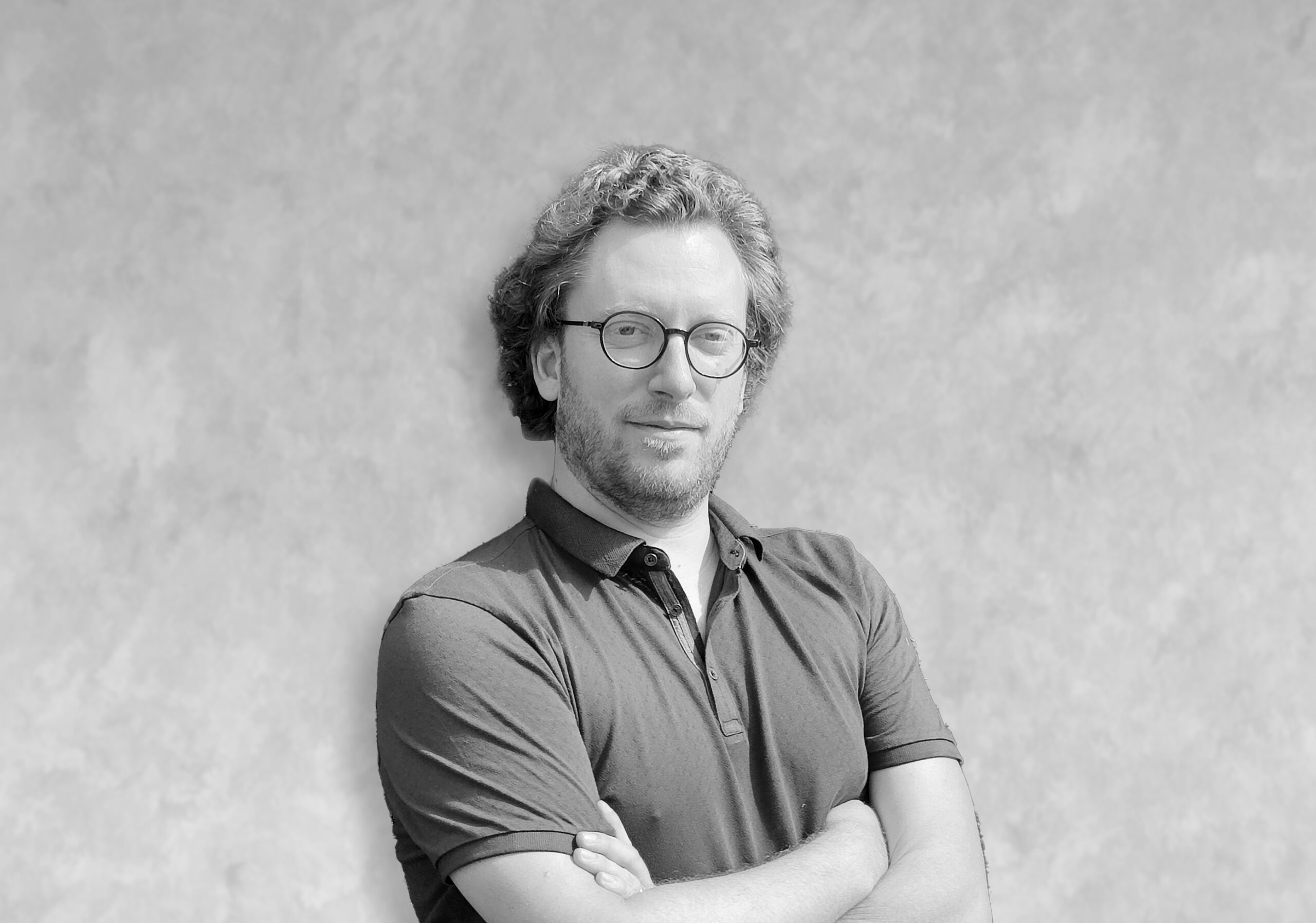 pierre Portrait en noir et blanc d’un homme en polo, bras croisés, devant un mur texturé