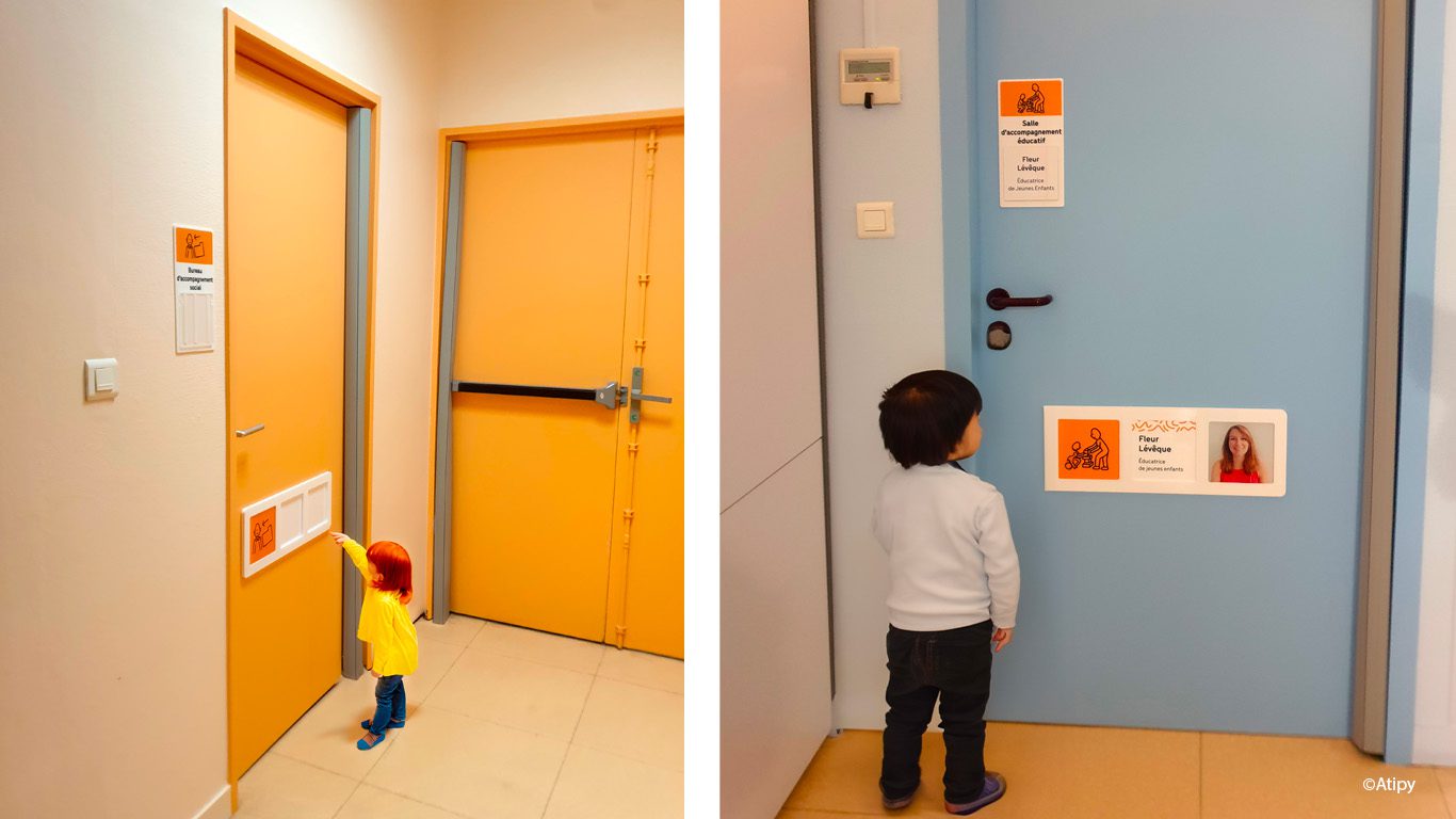 Enfant devant des portes colorées avec panneaux signalétiques illustrés et nom du personnel en établissement