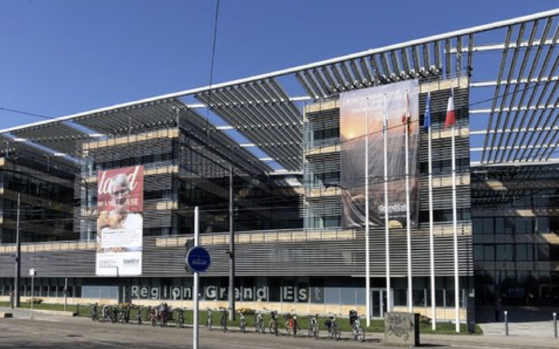 Façade vitrée du siège de la région Grand Est avec grandes bannières, mâts de drapeaux et vélos alignés