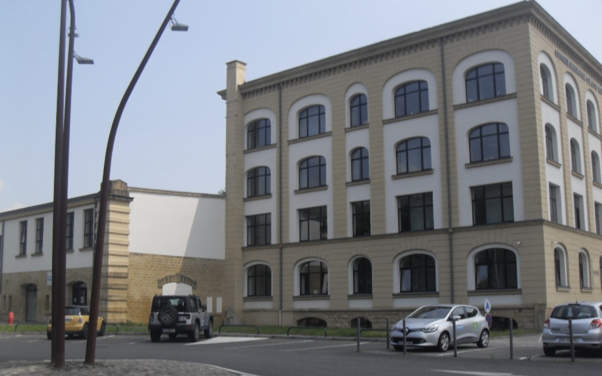 Bâtiment de bureaux à façades beige et blanche avec grandes fenêtres cintrées, vu depuis un parking