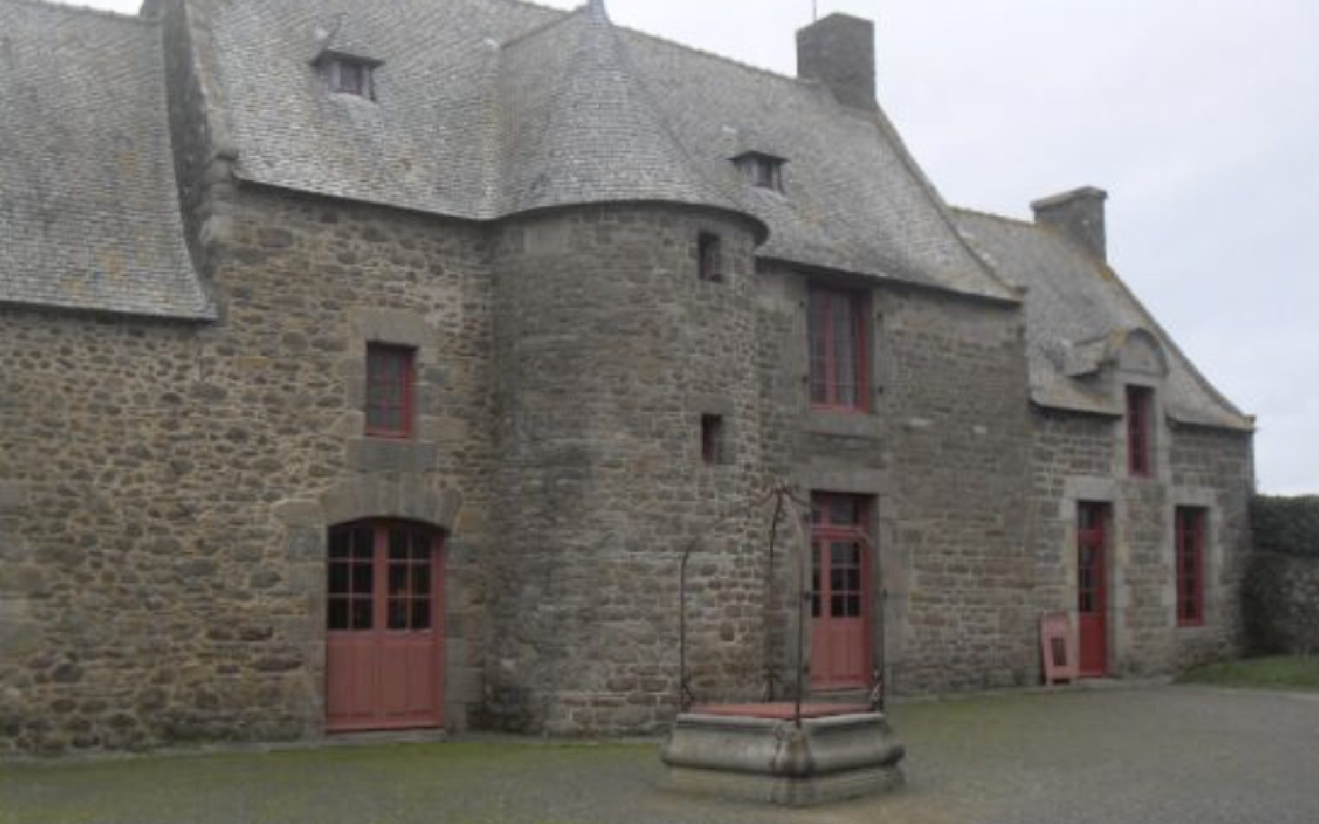 Façade en pierre d’un bâtiment ancien à Saint-Malo, avec tourelle centrale, portes rouges et cour pavée