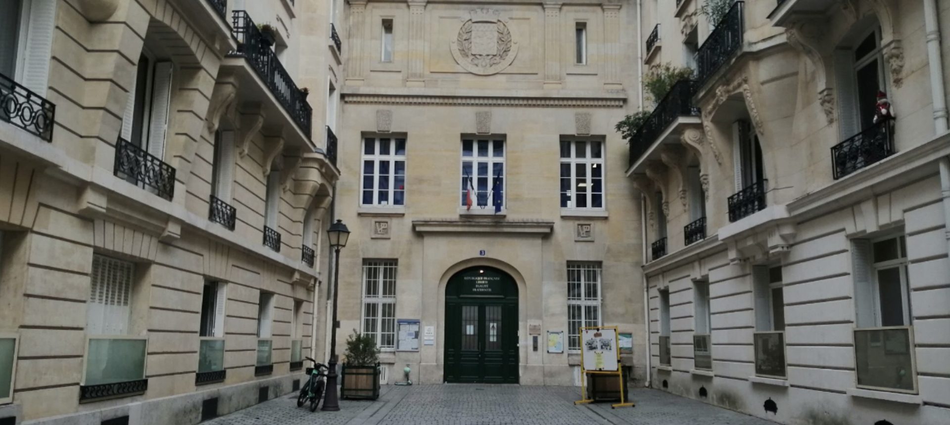 Cour intérieure d’un bâtiment de la Ville de Paris avec entrée centrale, drapeaux français et européen