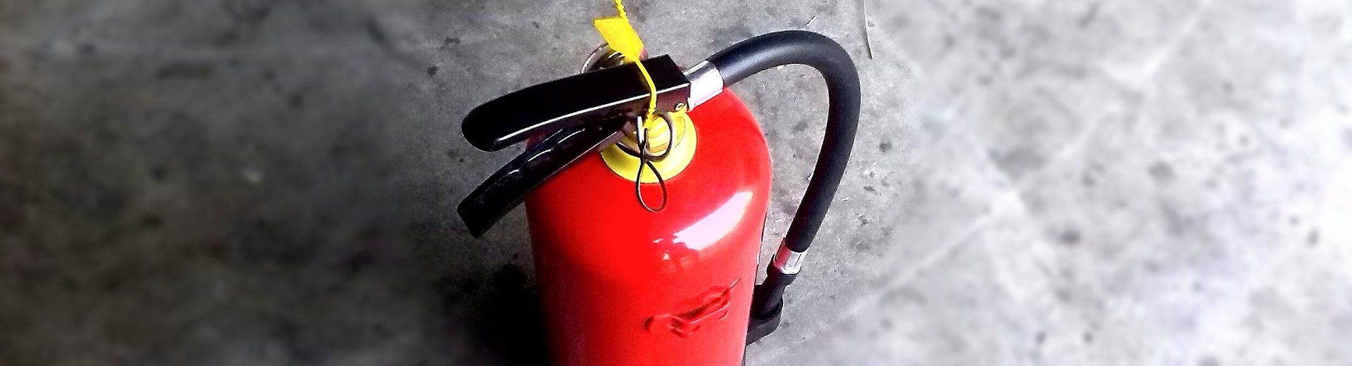 Extincteur rouge avec poignée noire et goupille jaune posé sur un sol en béton gris
