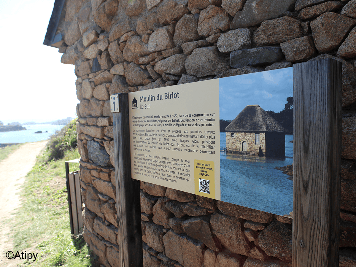 Visiteur devant un panneau sur le Moulin du Birlot le long d'un sentier côtier rocheux à Bréhat